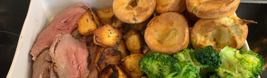 A roast beef dinner with roast potatoes, Yorkshire puddings and broccoli.