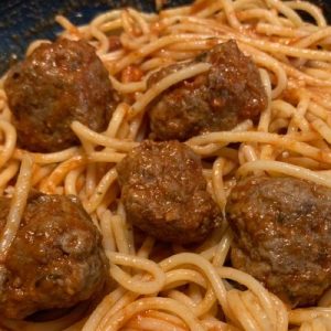 picture of a bowl of spaghetti topped with five meatballs.